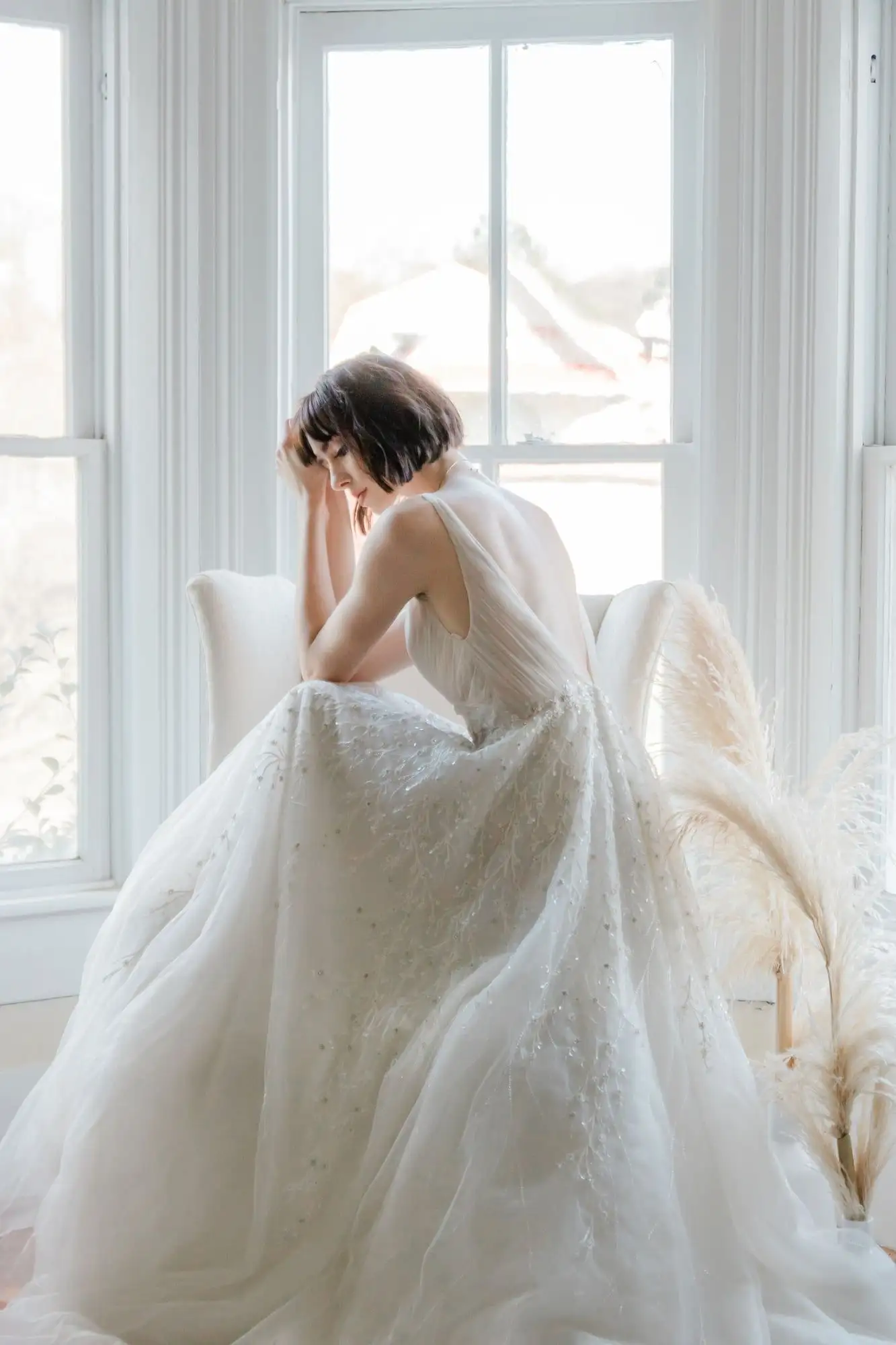 Vestido de novia corte princesa con pedrería y espalda descubierta, visto de espaldas con luz de ventana