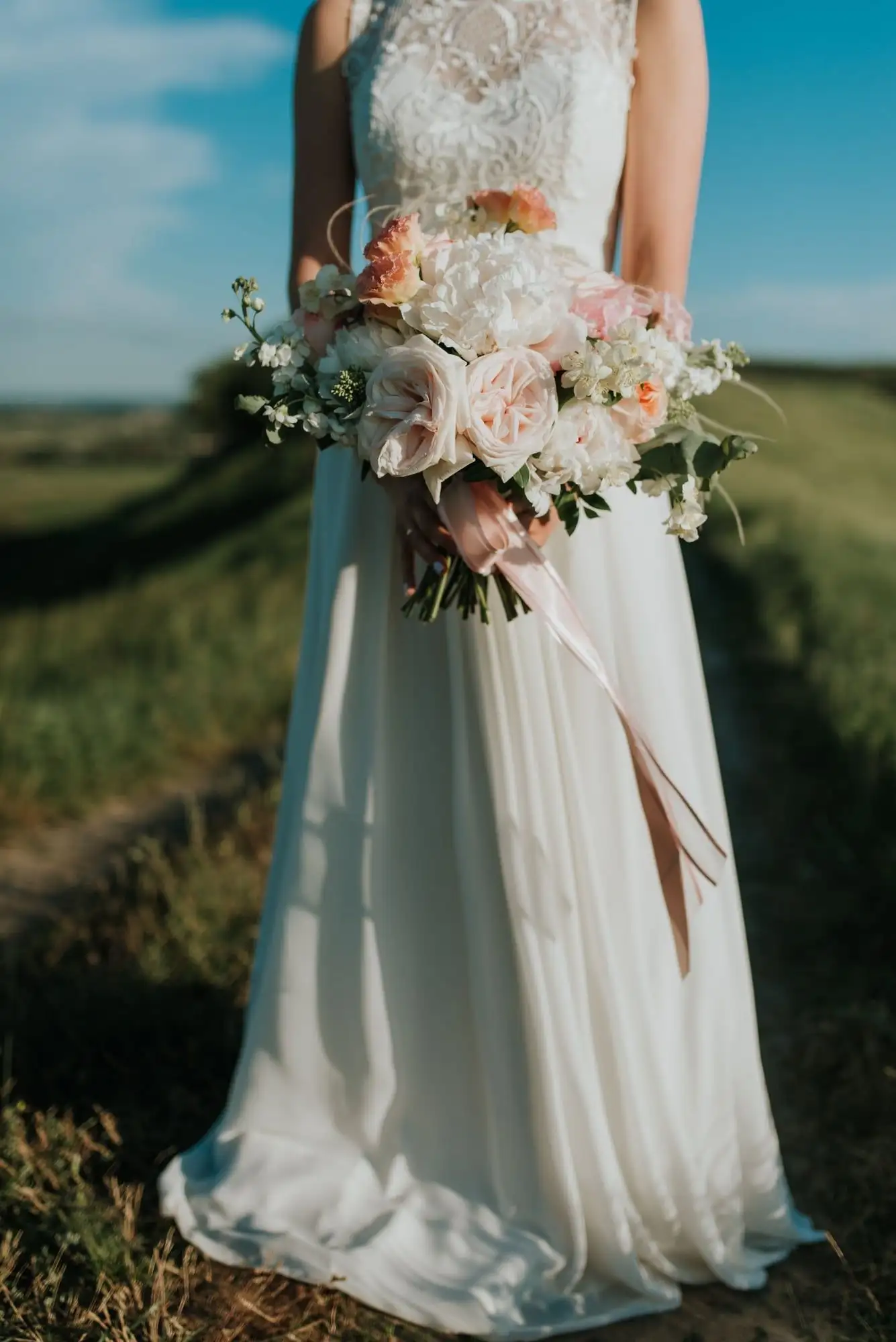 Vestido de novia con cuerpo de encaje y falda corte A, combinado con un ramo blanco y rosa pálido